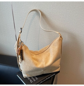 Detail of beige suede hobo bag with a decorative beaded tassel on a neutral background