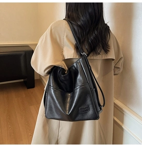 Black leather tote bag shown on shoulder of model wearing a trench coat for daily commute