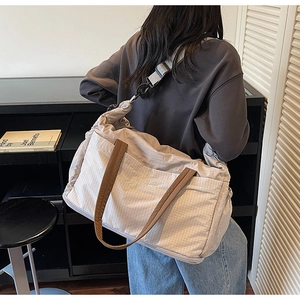 Detail of beige plaid tote bag with brown straps and detachable shoulder strap on a model