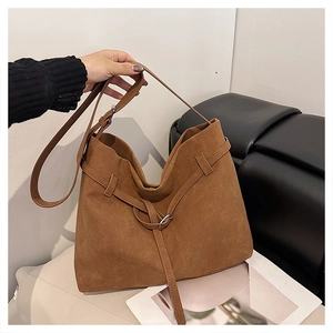 Detail of brown suede tote bag featuring adjustable strap and metallic buckle accents