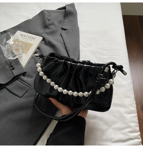 Close-up of black pleated cloud bag with glossy patent leather and pearl strap detail