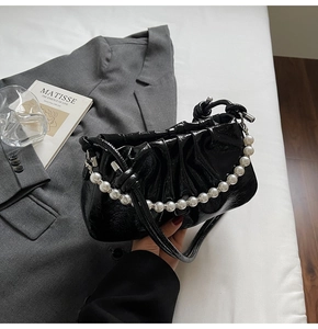 Detail of black pleated cloud bag featuring glossy patent leather and pearl chain strap