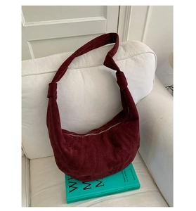 Detail of burgundy suede croissant bag with knot strap and stitching on a sofa