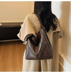 Detail view of brown leather tote bag with rectangular fashion logo label on model shoulder