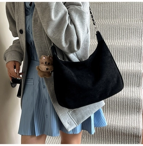 Detail of black suede hobo bag with metal chain strap and plush bear charm accessory