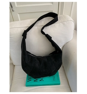 Detail of a large black suede croissant shoulder bag placed on a white leather sofa