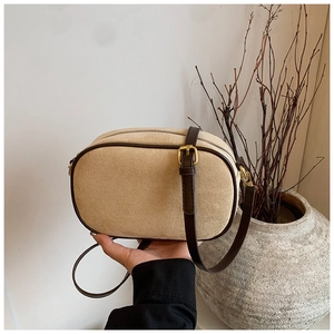 Detail of beige suede crossbody bag with dark brown leather trim and brass hardware
