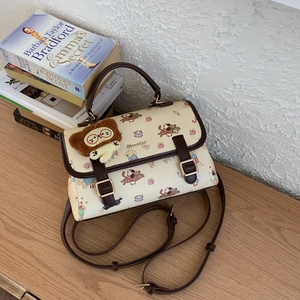 Gros plan d'un sac bandoulière crème avec motifs de chiens et pendentif en peluche