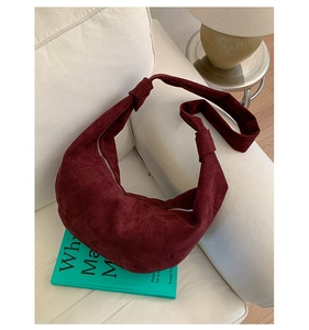 Close-up of burgundy suede croissant bag with curved stitching on a white sofa