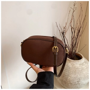 Detail of a brown suede camera bag with leather strap and gold hardware accents