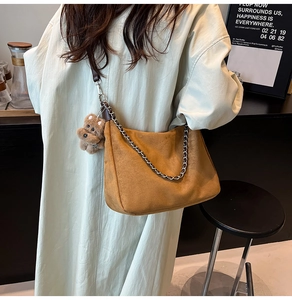 Detail of a brown suede crossbody bag with silver chain strap and a plush bear charm