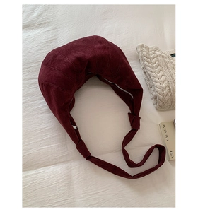 Detail of burgundy suede croissant bag with knotted strap on white textured fabric