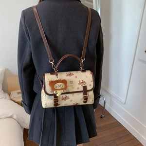 Détail du sac à dos crème avec motifs chiens, bordure en cuir et pendentif ours