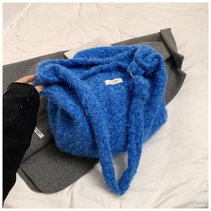 Détail du sac fourre-tout en tricot bleu roi duveteux avec étiquette sur lit blanc