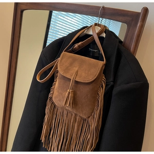 Détail d'un sac bandoulière en daim marron à franges sur un manteau en laine noir