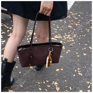 Outdoor shot of a brown quilted suede tote bag with wooden bead charm and thin straps