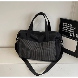 Detailed shot of a black nylon travel tote with grey checkered pocket and wide shoulder strap