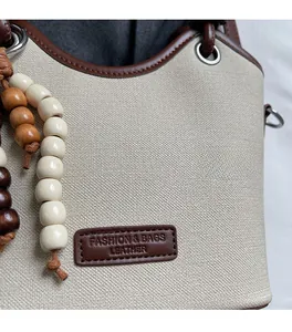 Gros plan du sac seau en toile crème avec bordure en cuir marron et breloque en perles