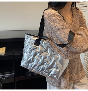 Detail of silver quilted tote bag featuring metallic finish and black shoulder straps