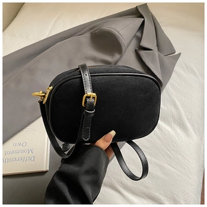 Detail view of a black matte crossbody bag featuring leather piping and gold metal buckles