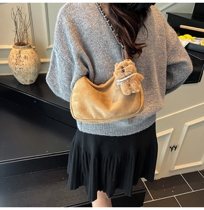 Detail of brown suede crescent bag featuring a gold chain strap and plush bear charm