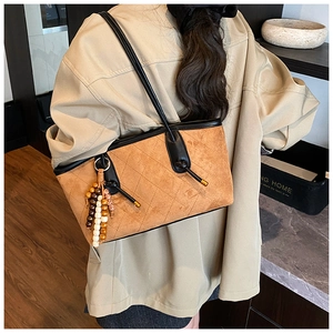 Detailed view of brown quilted suede shoulder bag with black trim and beaded charm