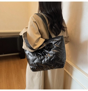 Detail of a black quilted puffer tote bag shown on a model in a minimalist style