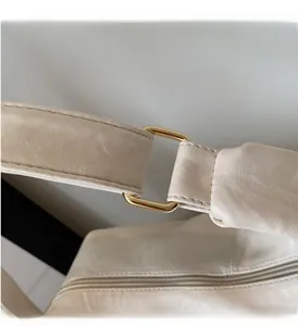 Close-up of golden metal buckle and leather strap on a cream crossbody dumpling bag