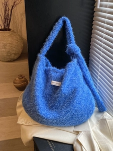 Blue fuzzy knit shoulder bag with logo patch on white blazer in a cozy room setting