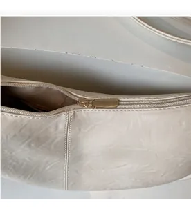 Detail view of the smooth golden metal zipper on the cream leather crossbody bag