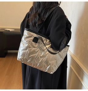 Silver quilted tote bag with black straps worn by a model in a minimalist interior setting