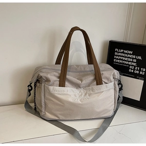 Detail of grey nylon tote bag showing side pocket, brown handles and logo on marble surface