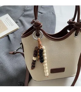 Détail du sac seau en toile beige avec garniture en cuir marron et pendentif perlé