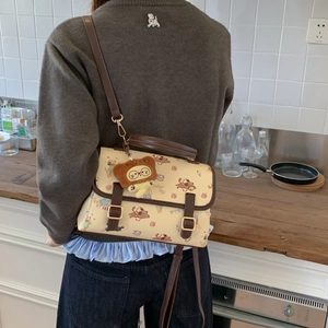 Détail d'un sac bandoulière beige avec motifs de chiens et breloque en peluche d'ours