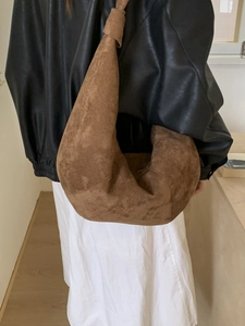 Brown suede crescent shoulder bag with knot strap detail shown on a stylish model