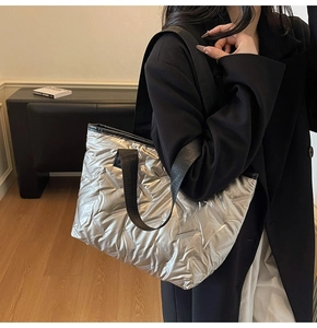 Detail of silver quilted tote bag featuring padded nylon texture and black wide shoulder strap