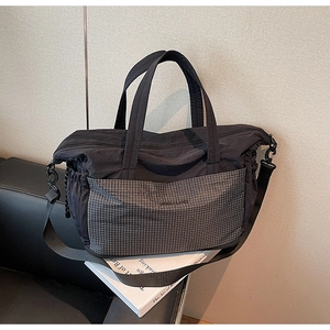 Macro shot of large black quilted tote bag with gray plaid pocket on a leather sofa