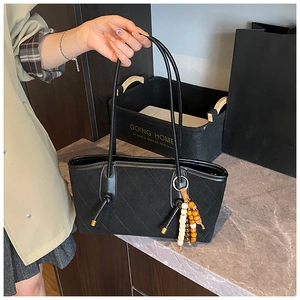 Detail of black quilted leather tote bag featuring unique wooden bead pendant on handle