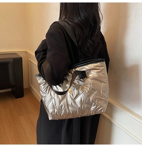 Silver quilted tote bag with black straps worn by model in a minimalist home setting