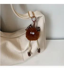 Close-up of a plush brown ball charm with a leopard bow on an off-white leather bag