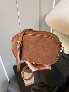 Brown matte suede oval crossbody bag with gold hardware shown in a cozy home setting