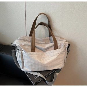 Detail view of light grey nylon tote bag featuring brown straps and side drawstring design