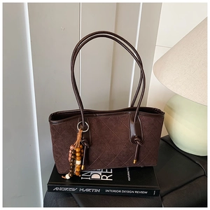 Detail of dark brown quilted suede handbag with ethnic wooden bead tassel on a book