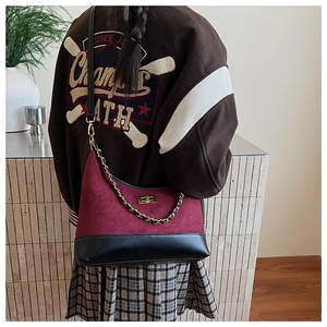Detail of burgundy quilted dumpling bag with gold twist lock and chain strap on shoulder