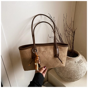 Detail of khaki quilted tote bag with brown leather trim and beaded charm pendant