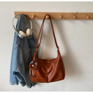 Brown leather hobo shoulder bag with leopard plush charm on a wooden clothes rack
