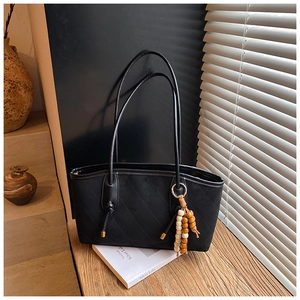 Detail of black quilted tote bag with unique wooden bead charm on a wooden table