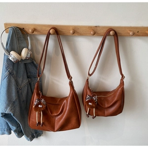 Brown faux leather half-moon bags in two sizes with plush charms on wooden wall hooks