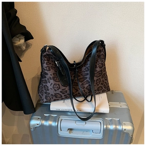 Leopard print tote bag with black leather straps styled on a silver suitcase