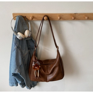 Brown faux leather hobo bag with a leopard print plush charm hanging on a wooden hook